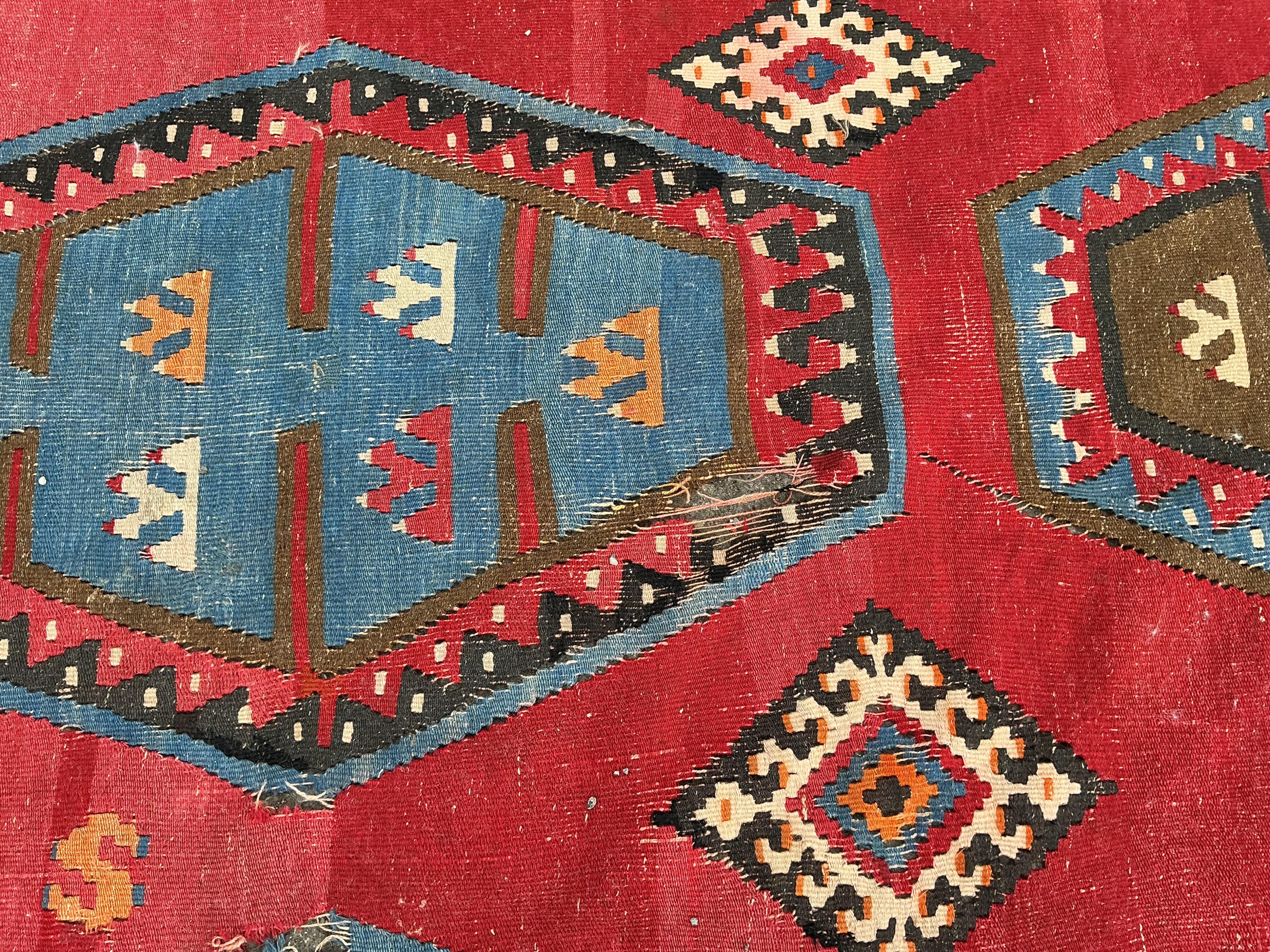 A Turkish Kilim flatweave polychrome carpet, woven with three rows of hexagons, on a red ground, (severely holed and damaged in places), 373 x 267cm